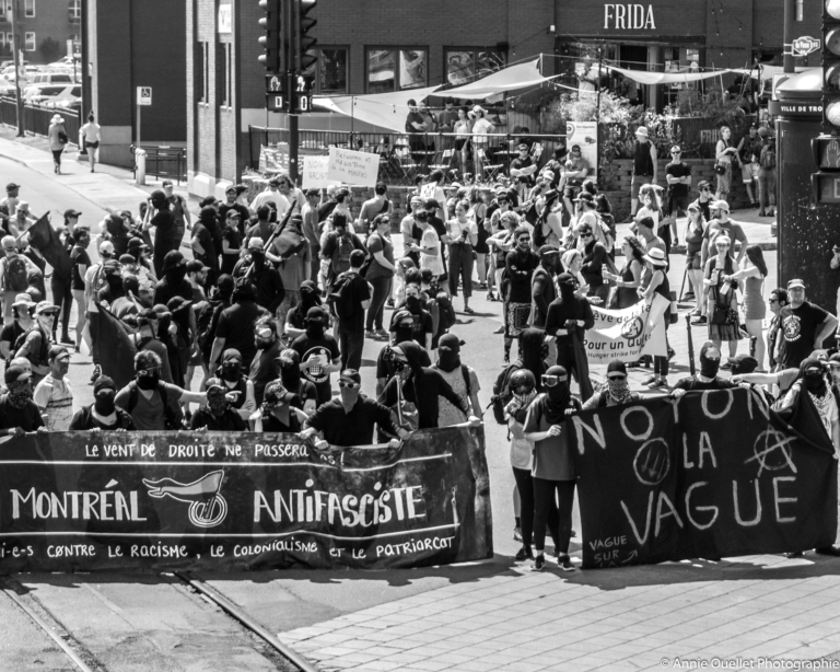 Protesters gathered in the street with banners, including one at front that reads "Montréal Antifasciste"