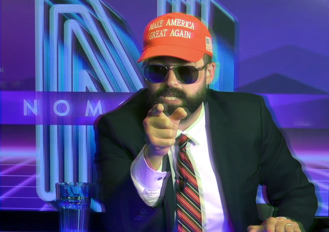 Man in jacket, tie, shades, and "Make America Great Again" cap pointing at the camera