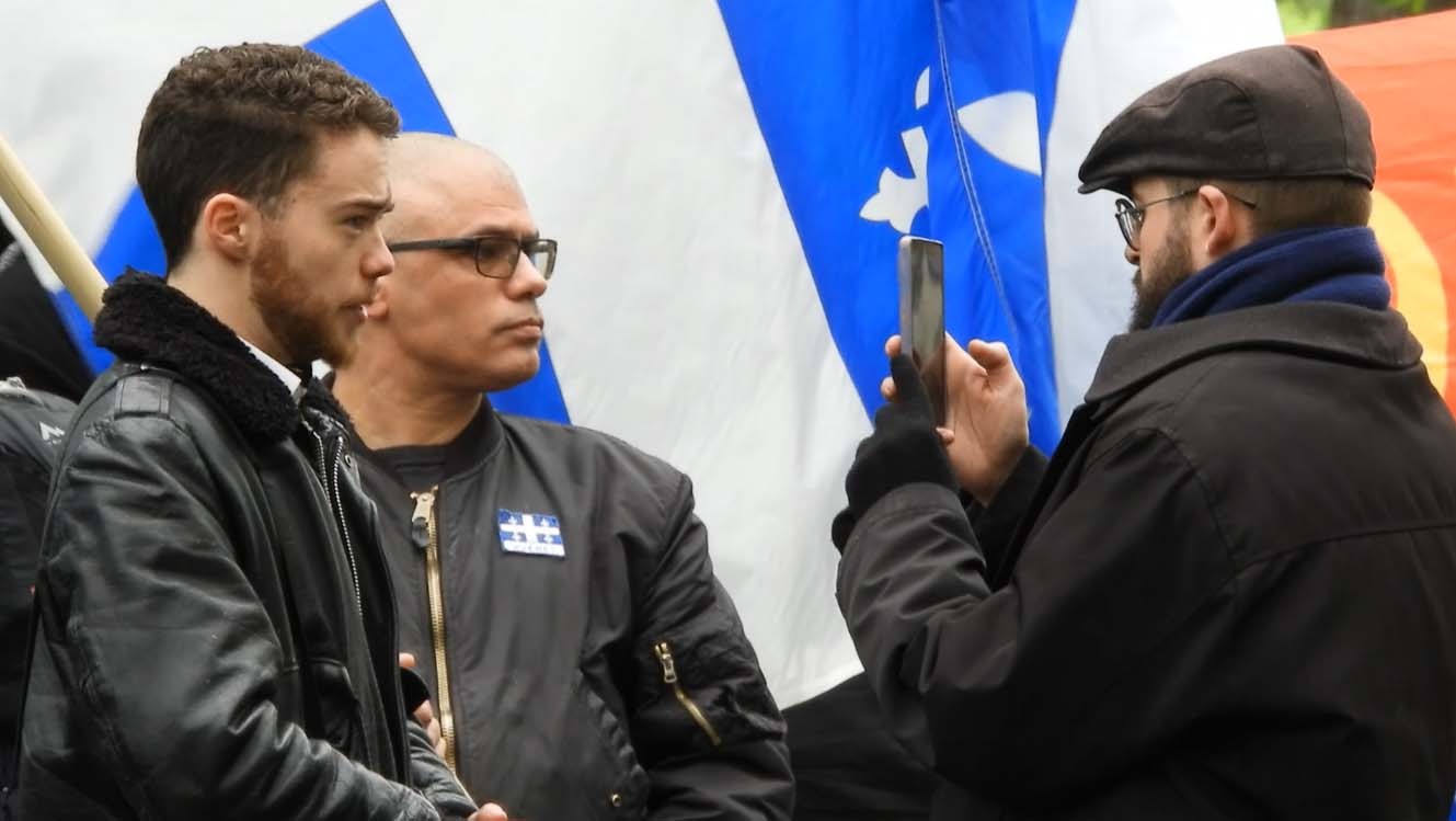 Man at right takes phone photo of two men at left.