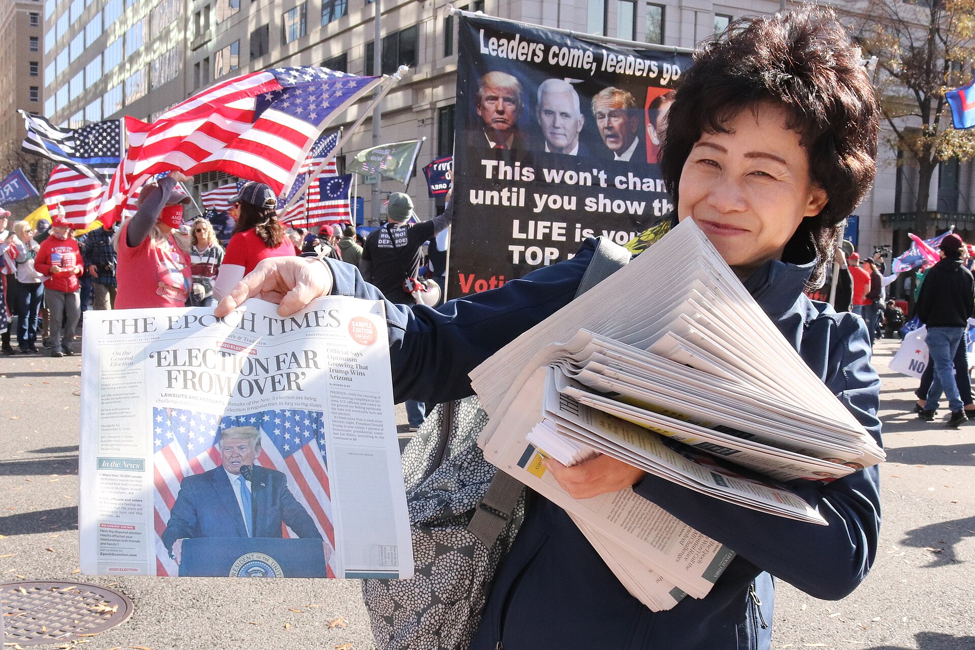 Woman at MAGA rally holding copies of Epoch Times newspaper